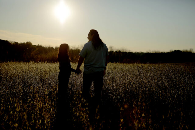 A man and his daughter hold hands in a field.