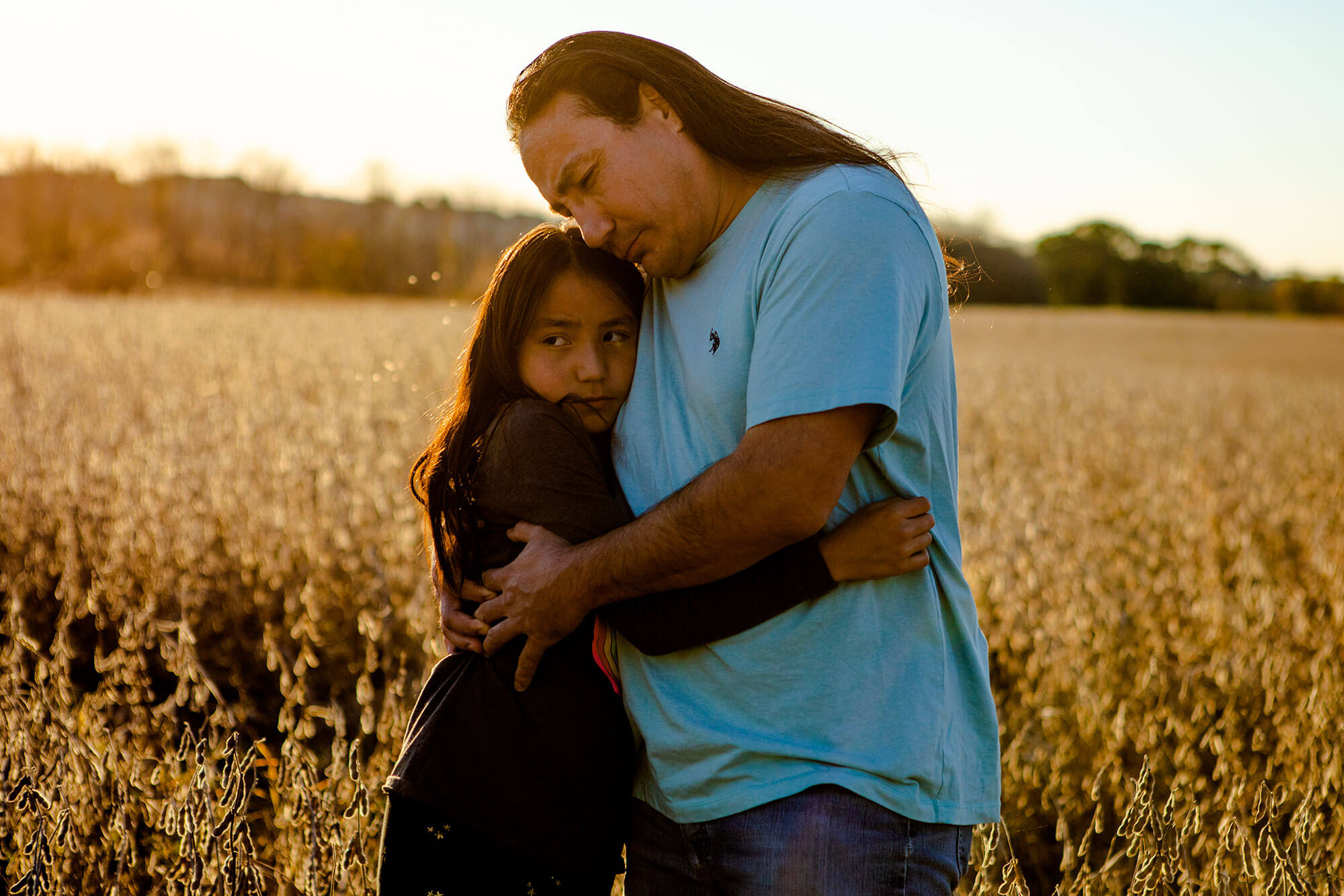 A Native American man hugs his daughter in a field.