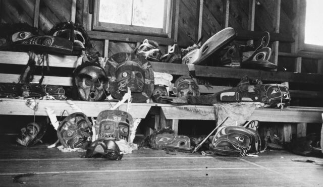A Kwakwa̱ka̱ʼwakw Sun Mask (centre) pictured among other Potlatch regalia that was surrendered under duress in Parish Hall, Alert Bay, BC in 1922
